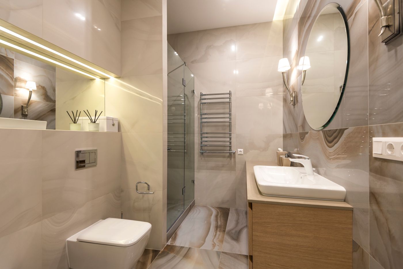 Renovated bathroom with marble tiling, a round mirror and warm lighting